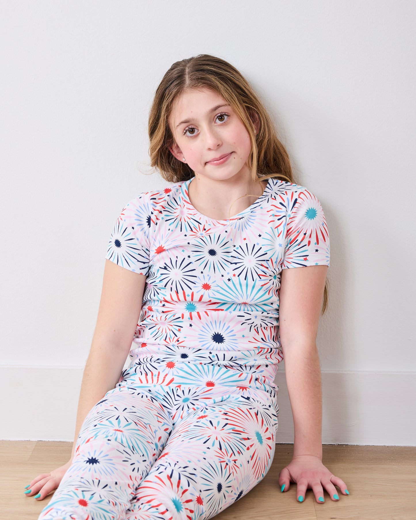 Child model seated in the fireworks-print short-sleeve pajama top and matching pants