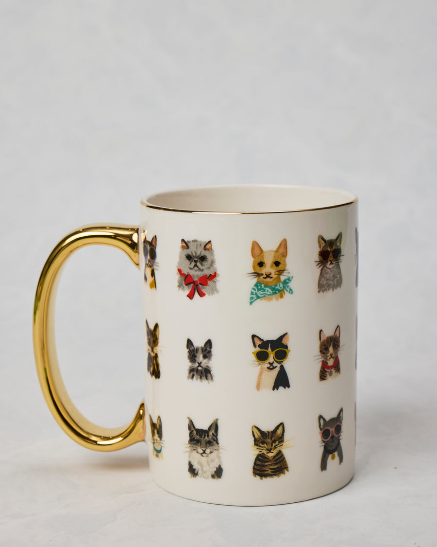 Porcelain Cool Cats mug shown from the side with a gold handle, gold rim, and rows of illustrated cats wearing accessories.