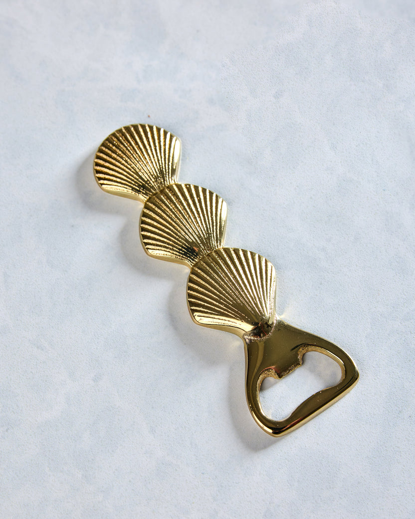 Angled view of the brass bottle opener with three ridged seashell shapes