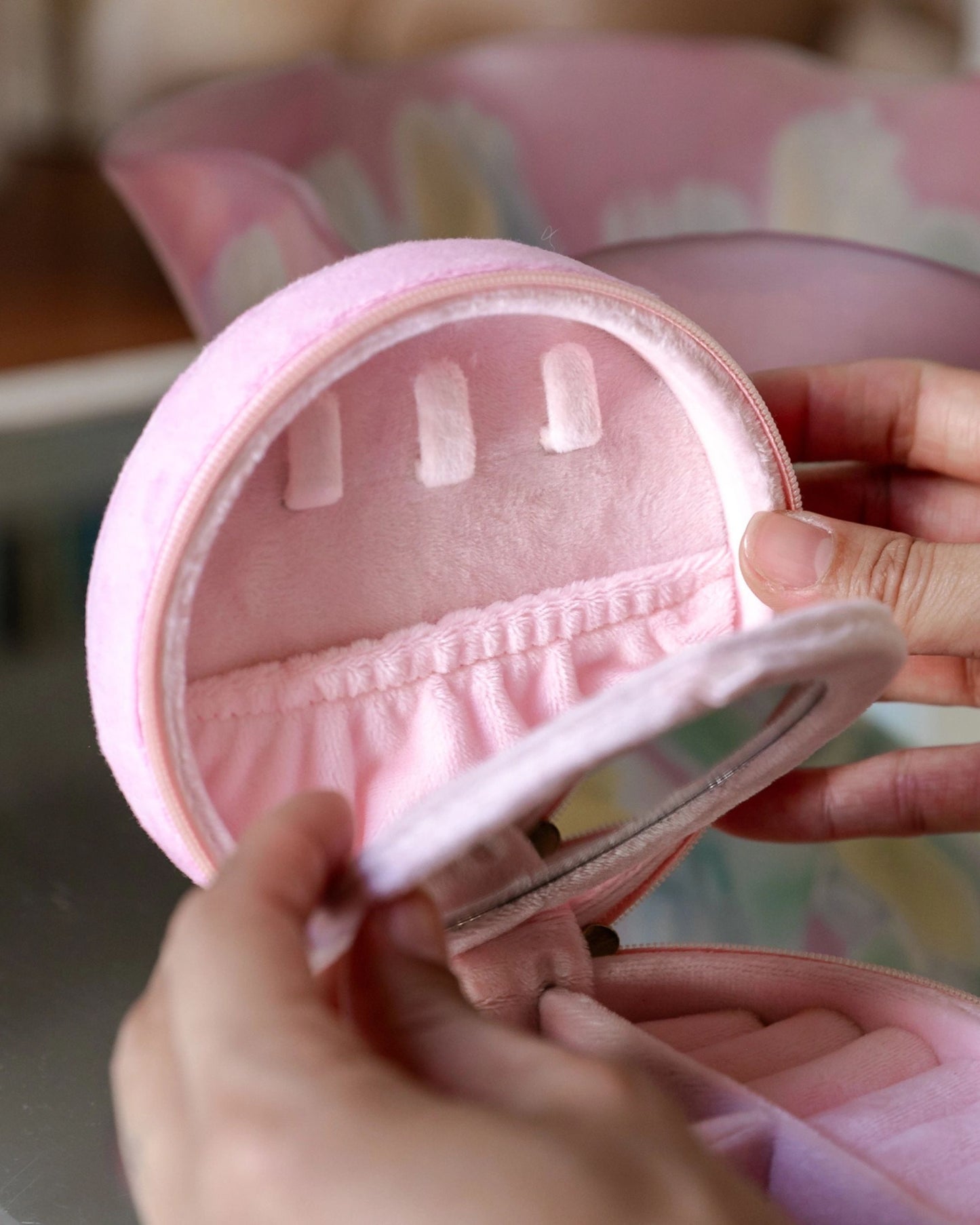 Hands opening a pink round jewelry case to show its interior pocket and ring slots.