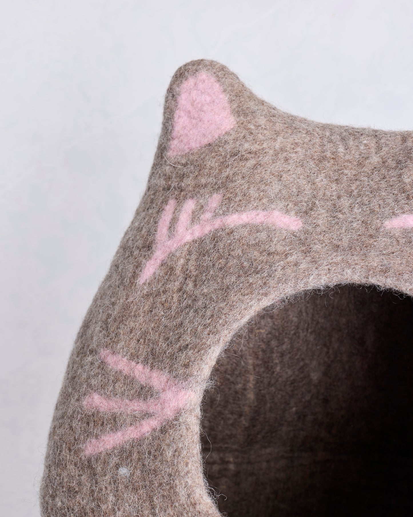 Close-up of the cat cave bed's pointed ear, pink facial details, wool texture, and entrance edge