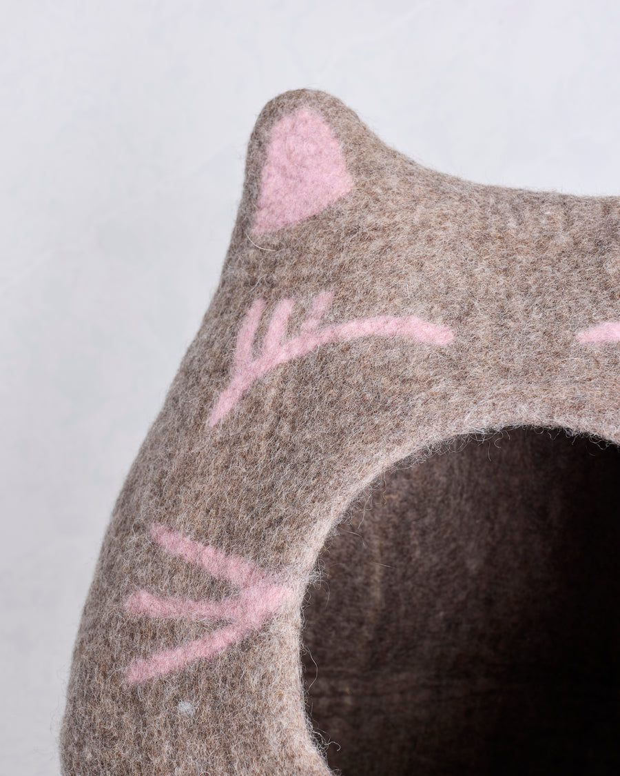 Close-up of the cat cave bed's pointed ear, pink facial details, wool texture, and entrance edge