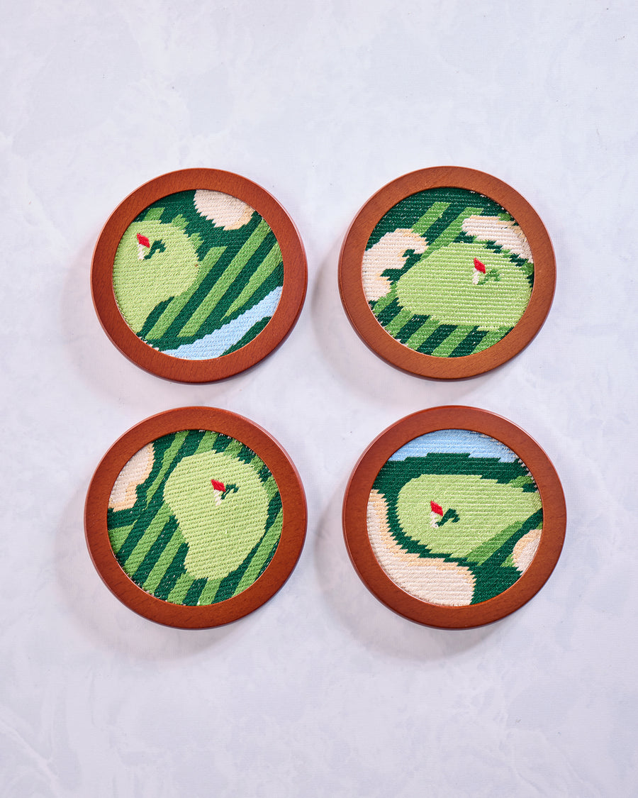 Four round green stitched golf coasters arranged in a two-by-two layout, each with a red flag design.