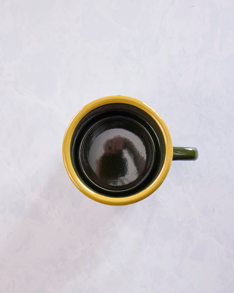 Top view looking into the empty green enamel mug with a yellow rim and black interior