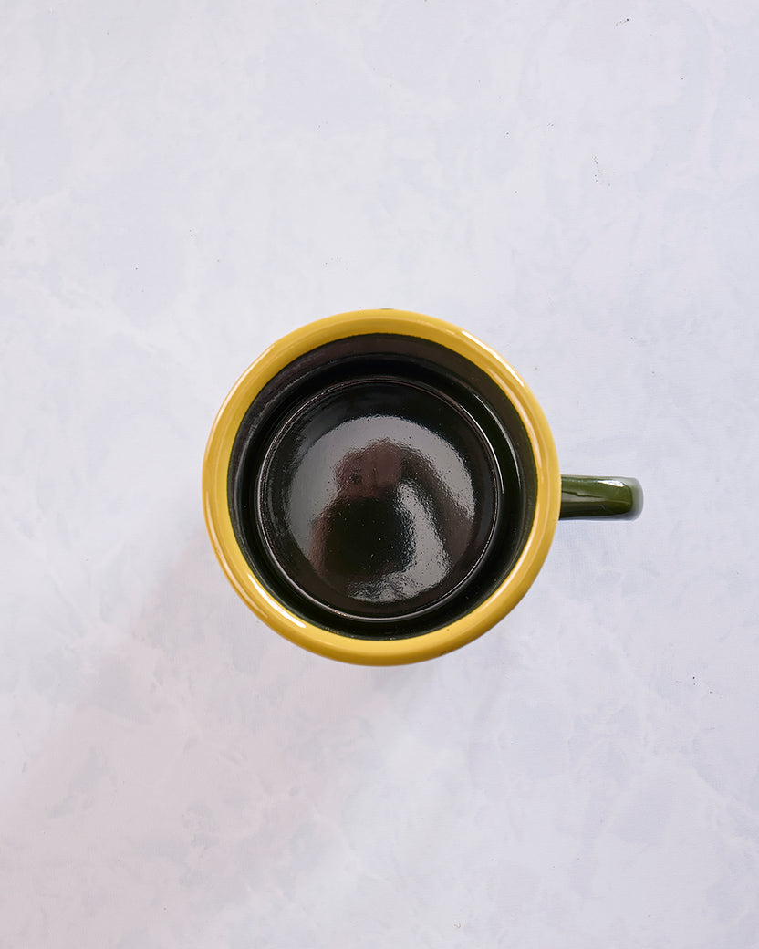 Top view looking into the empty green enamel mug with a yellow rim and black interior