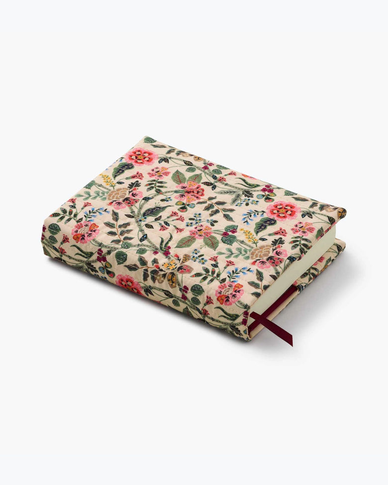 Closed Gracie journal shown at an angle with a cream floral quilted cover and red ribbon bookmark.