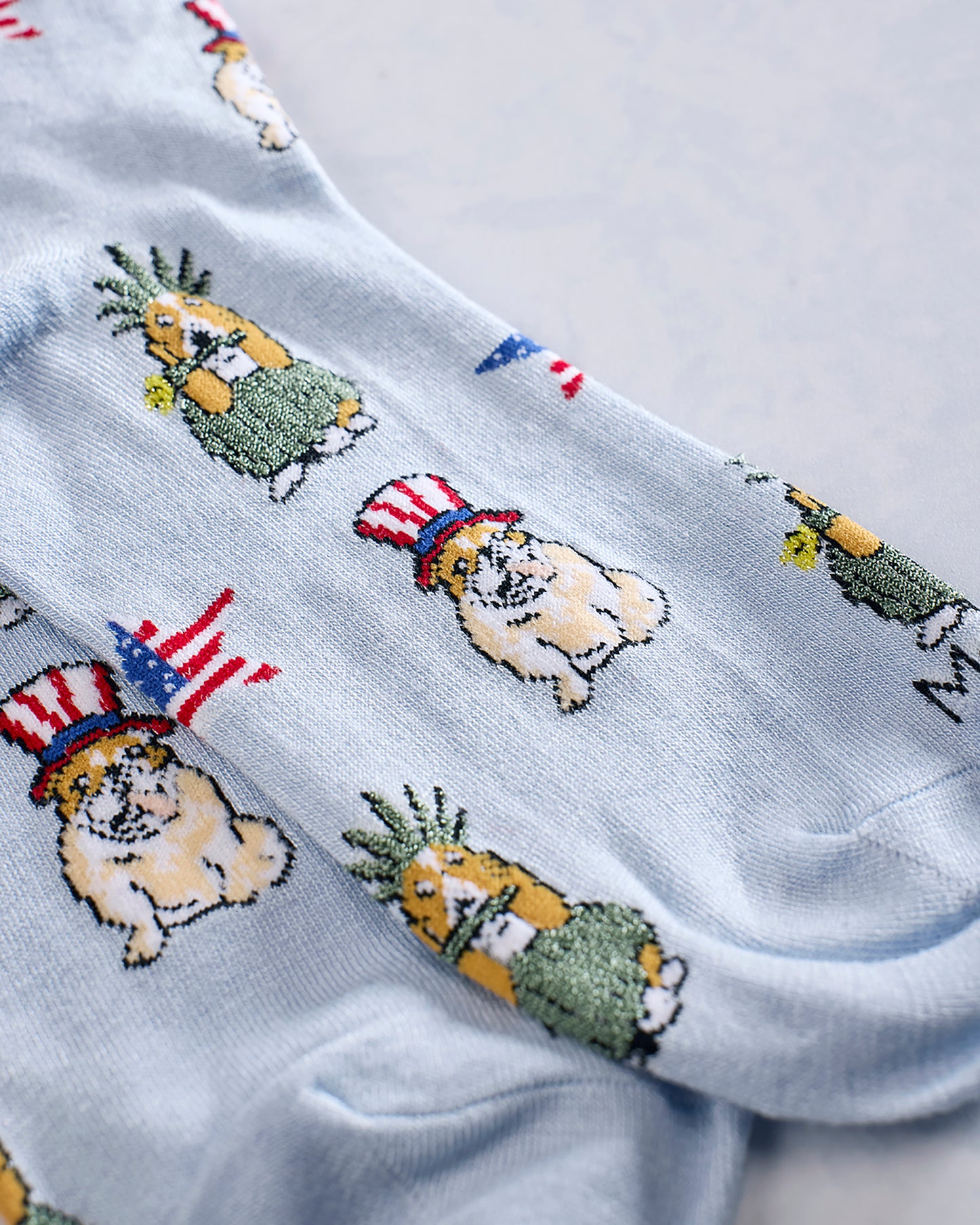 Close-up of light blue socks showing dogs wearing patriotic hats and pineapple-like figures in the printed pattern.
