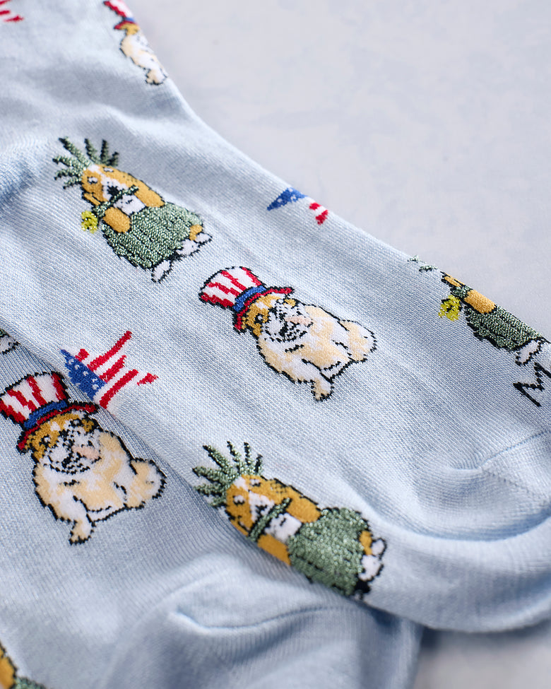 Close-up of light blue socks showing dogs wearing patriotic hats and pineapple-like figures in the printed pattern.