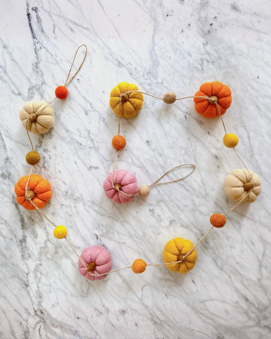 Pumpkin garland arranged in a loose circle, with orange, yellow, pink, and cream pumpkins connected by string.