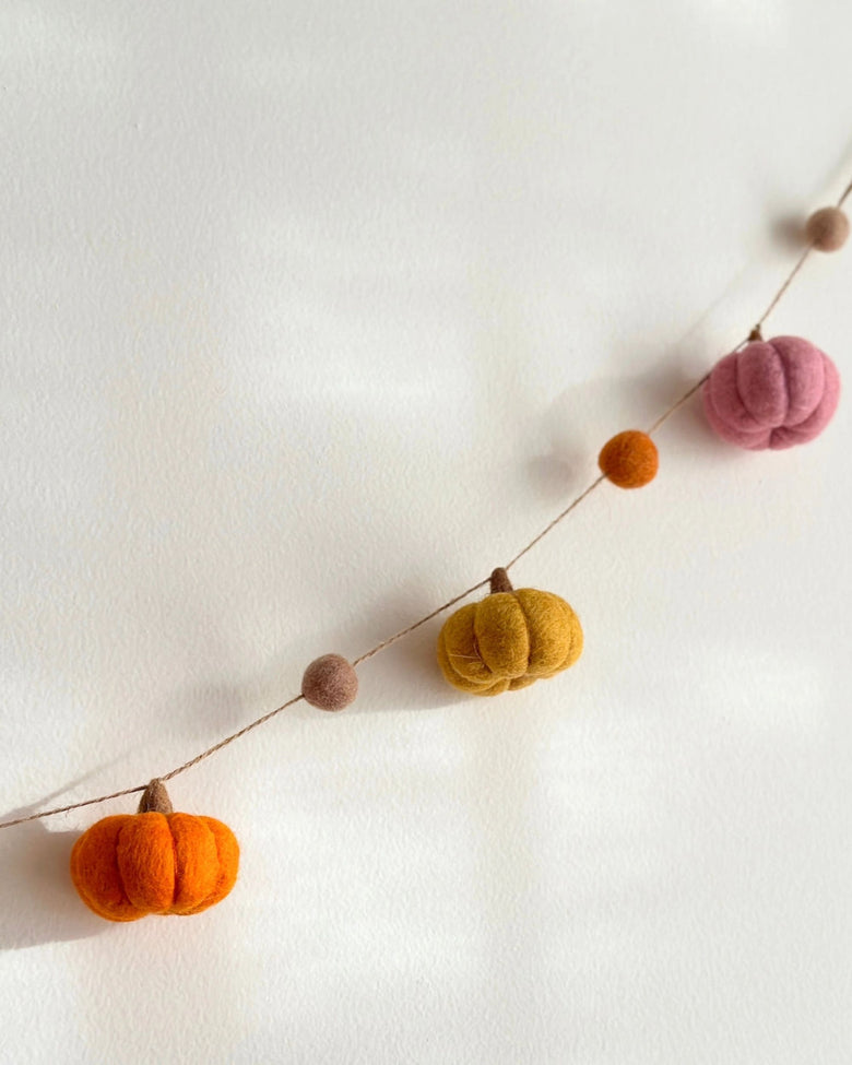Felt pumpkin garland with orange, yellow, pink, and small brown pumpkins strung diagonally on a wall.