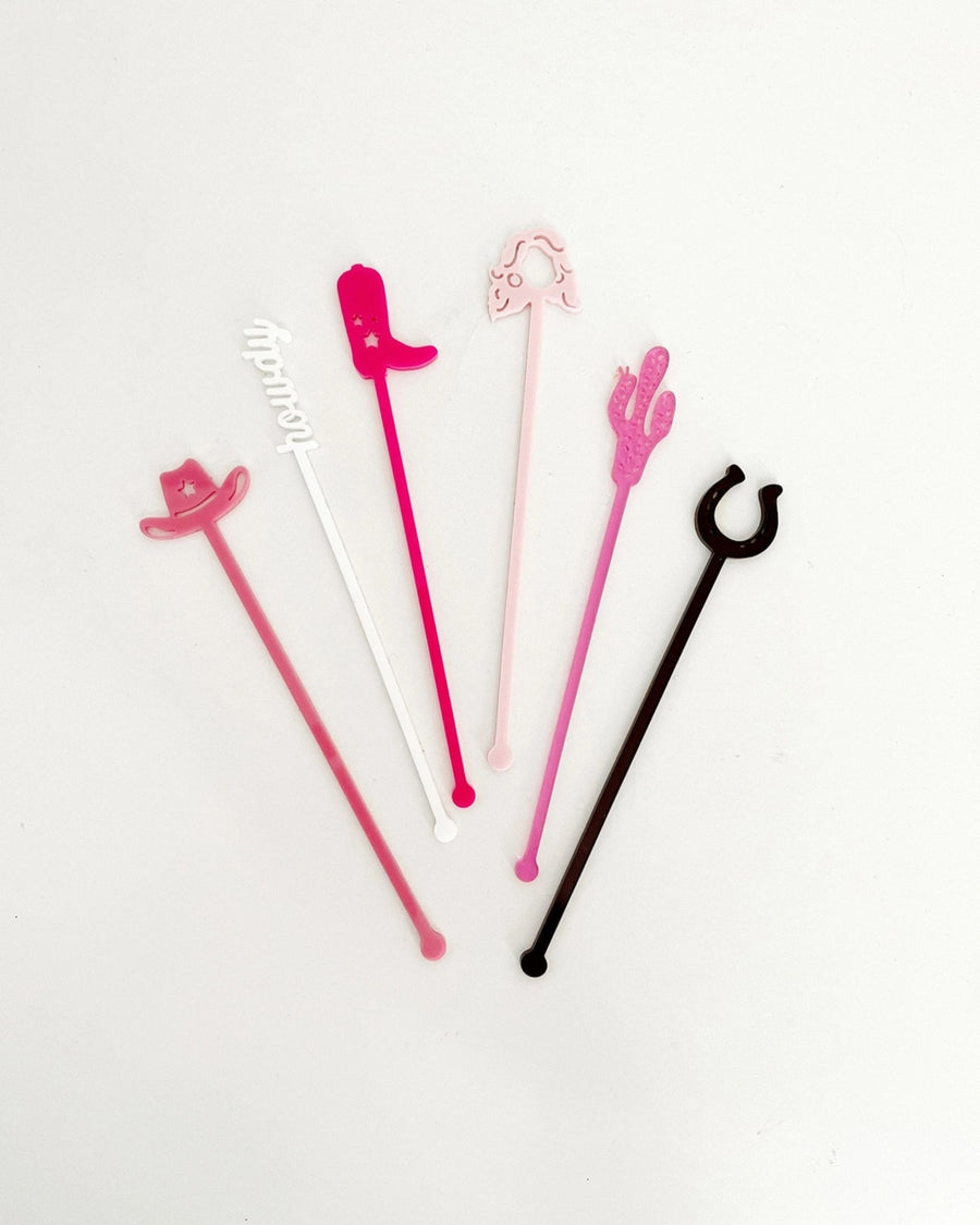 Six colorful Western-themed stir sticks arranged on a white background, including cowboy hats, a boot, a cactus, a horseshoe, and a white script-shaped design.