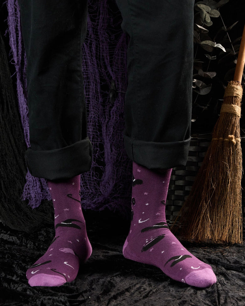 Purple patterned socks worn with black pants, showing broomsticks, witch hats, stars, and crescent moons.
