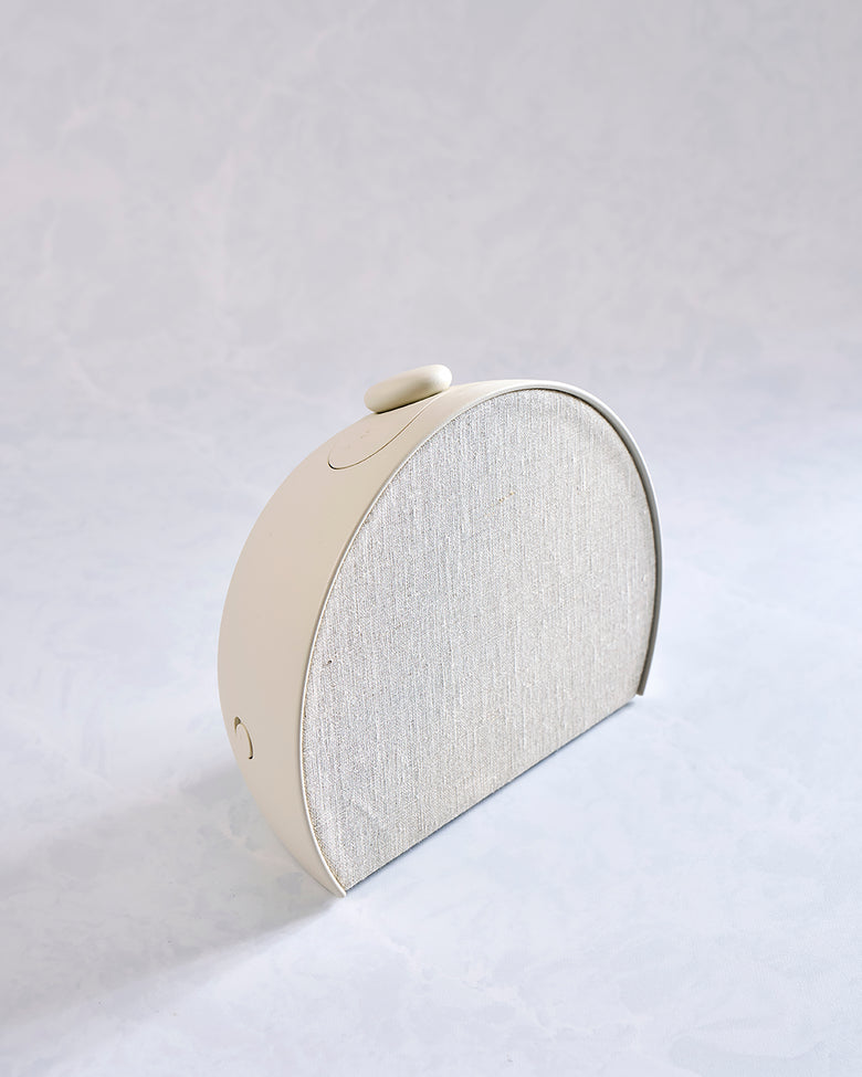 Angled side view of the putty-colored Restore 3 sunrise alarm clock with a light fabric front grille and top control button.