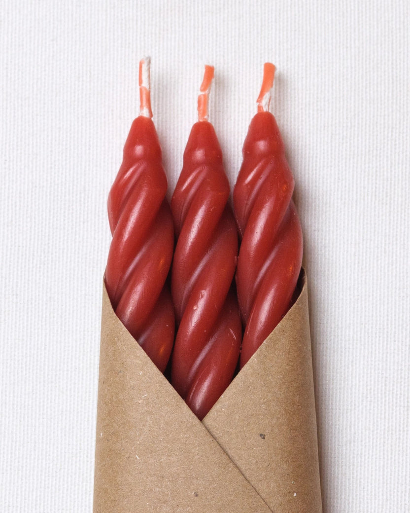 Close view of three rose-colored spiral candles with exposed wicks in a kraft-paper sleeve.