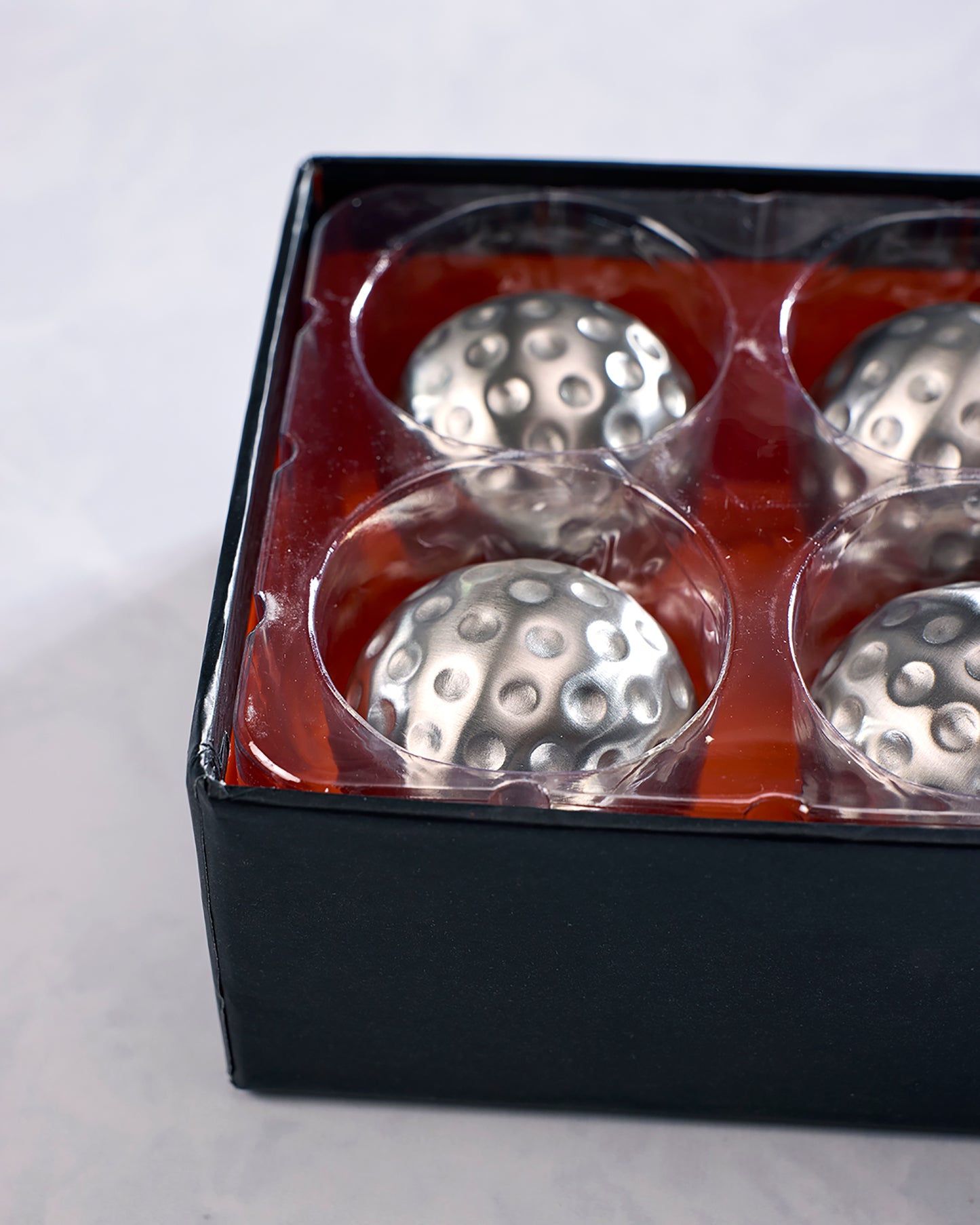 Close-up of four silver dimpled chilling cubes in the open black package tray.