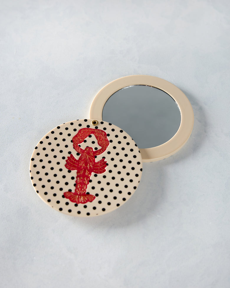 Open lobster compact mirror showing the reflective mirror and cream-and-black polka-dot cover with red lobster design.