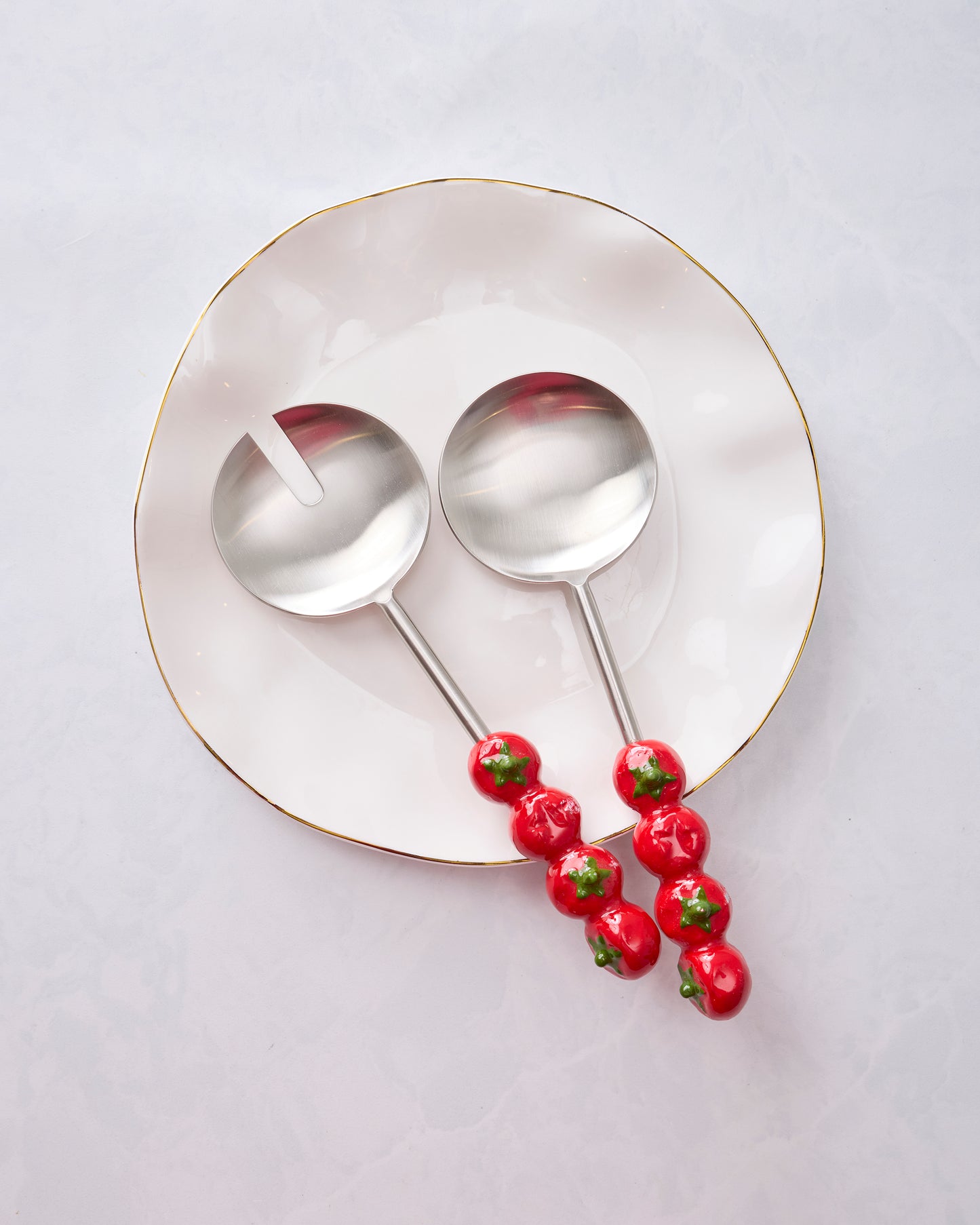 Tomato-handle salad servers placed side by side on a round plate