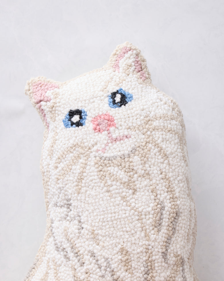 Close-up of the white cat-shaped hook pillow front with pink ears and nose, blue eyes, and stitched whiskers