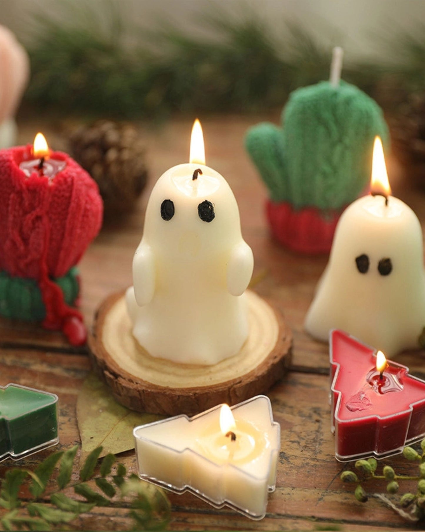 Lit white ghost-shaped candles displayed with colorful candles and greenery on a wooden table.
